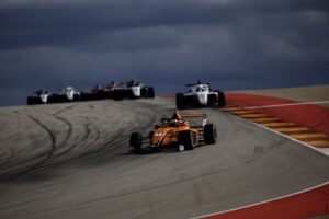 Monoplaza naranja liderando la carrera en una curva con otros coches al fondo